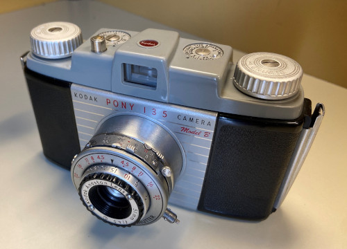 A front view of a Pony 135, showcasing 4 sets of numbers on the lens piece, a non-SLR viewfinder and all the nobs and dials on the top.