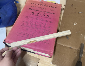 First straightedge that was tested, held up by a proud and sawdusty hand, with the book of Mathematical Instruments artfully in the background.